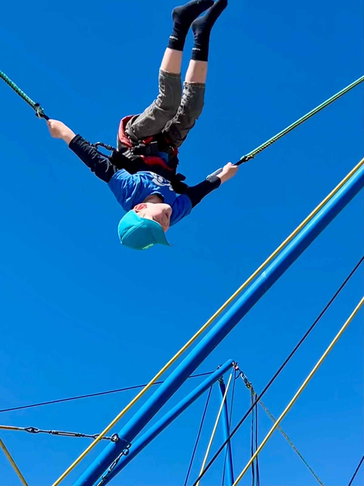 Kind macht Salto am gelb-blauen Bungee-Trampolin