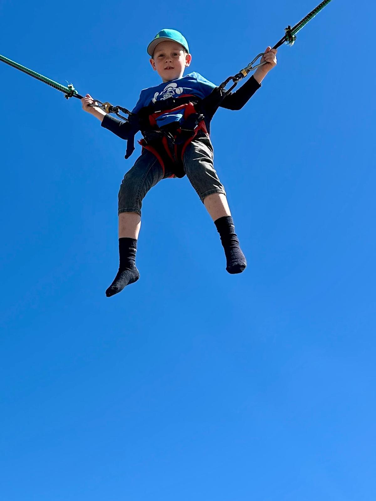 Kind fliegt hoch am Bungee-Trampolin unter blauem Himmel